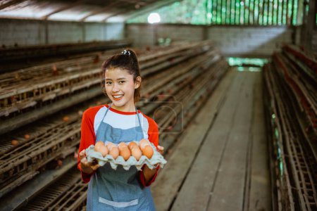 Téléchargez les photos : Souriant asiatique femme travailleur portant un plateau d'œufs d'une ferme de poulet - en image libre de droit