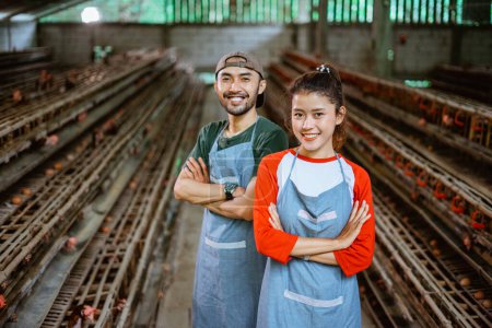 Téléchargez les photos : Attrayant asiatique femme et mâle agriculteur souriant avec les mains croisées debout dans une ferme avicole - en image libre de droit