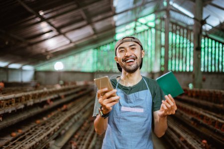 Téléchargez les photos : Heureux entrepreneurs asiatiques travaillent avec les smartphones et les livres de banque sur les fermes de poulet - en image libre de droit