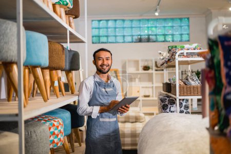 Téléchargez les photos : Homme commerçant souriant regardant la caméra tout en utilisant une tablette dans le magasin de meubles - en image libre de droit