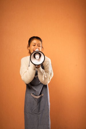 Téléchargez les photos : Femme asiatique portant tablier annonçant avec mégaphone en arrière-plan isolé - en image libre de droit