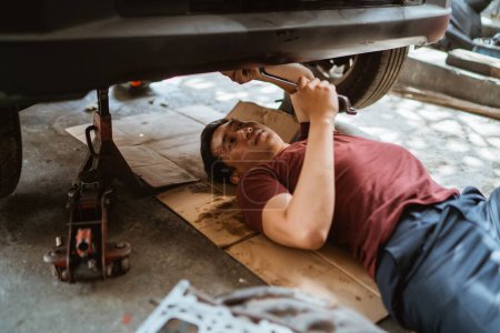 Téléchargez les photos : Jeune mécanicien couché et travaillant voiture de service de train d'atterrissage au garage - en image libre de droit