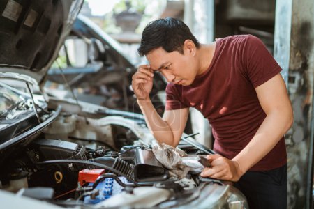 Téléchargez les photos : Un jeune mécanicien masculin est confus lorsqu'il travaille sur une machine dans un atelier de réparation - en image libre de droit