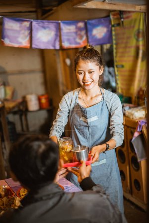 Foto de Mujer asiática tendero usando delantal sirve comida a los clientes en un puesto tradicional - Imagen libre de derechos