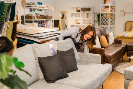 Téléchargez les photos : Belle femme commerçante arrangeant des coussins de canapé avec des lettres d'amour dans le magasin de meubles - en image libre de droit