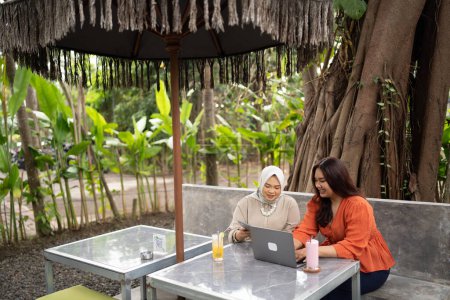 Téléchargez les photos : Deux femmes discutent du travail ensemble dans un café en utilisant une tablette et un ordinateur portable - en image libre de droit