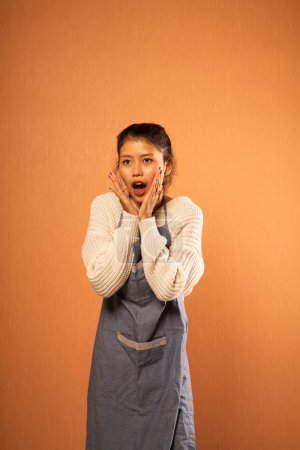 Téléchargez les photos : Jeune femme asiatique portant tablier avec expression surprise en arrière-plan isolé - en image libre de droit