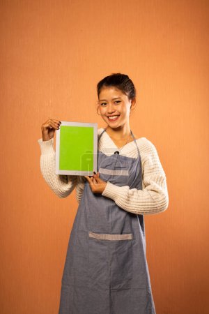 Téléchargez les photos : Sourire asiatique fille portant tablier tenant tablette numérique vierge avec fond isolé - en image libre de droit