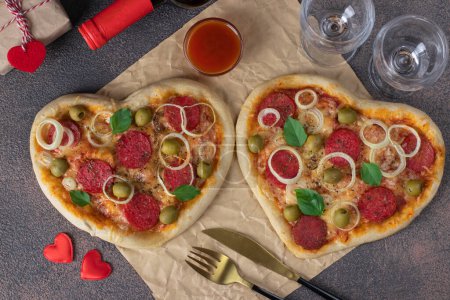 Two heart shaped pizza with salami sausage and cheese for Valentines Day on brown background
