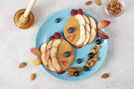 Fischpfannkuchen mit Pfirsichen, Beeren, Müsli und Mandeln auf blauem Teller, gesunde Frühstücksidee für Kinder