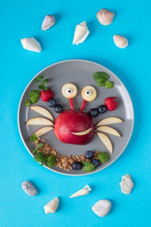 Sea crab made from fruits and berries such as apple, strawberry and blueberry - on blue background, Top view