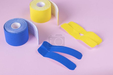 Rolls kinesiology tape in shape of letters X and V for lymphatic drainage on pink background
