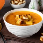 Pumpkin puree soup with orange, served in a white bowl with croutons