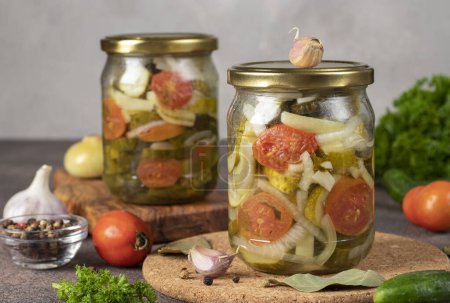 Téléchargez les photos : Salade de concombres marinés aux tomates et poivrons dans deux bocaux sur fond gris - en image libre de droit