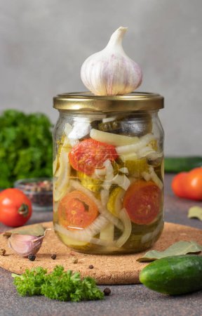 Téléchargez les photos : Salade de concombres marinés aux tomates et poivrons doux dans un bocal en verre sur fond gris - en image libre de droit