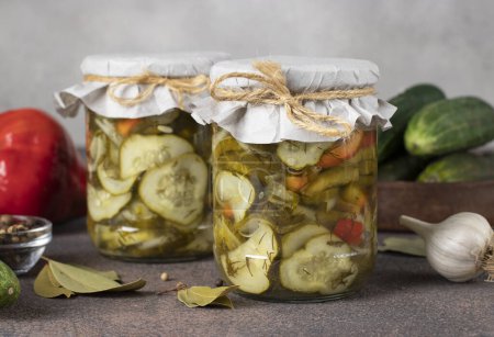 Téléchargez les photos : Pickled cucumbers salad with sweet peppers and onions in two jars on gray background - en image libre de droit