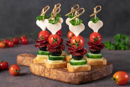 Foto de Canapé con queso, tomates cherry, salchichas y aceitunas negras sobre tabla de madera, Primer plano - Imagen libre de derechos