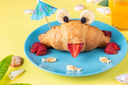 Fun food for kids - crab shaped croissant with strawberry and banana on blue plate on yellow background