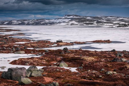 Téléchargez les photos : Hut at the waterfront of a frozen lake in the landscape of Hardangervidda National Park in Norway, snow and ice on the ground - en image libre de droit