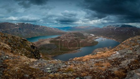 Foto de Turquoise and blue lakes in mountain landscape from above the hike to Knutshoe summit in Jotunheimen National Park in Norway, mountains of Besseggen in background, dark cloudy sky, moss in foreground - Imagen libre de derechos