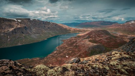 Foto de Blue lake in mountain landscape from above the hike to Knutshoe summit in Jotunheimen National Park in Norway, mountains of Besseggen in background, cloudy sky, moss in the foreground - Imagen libre de derechos