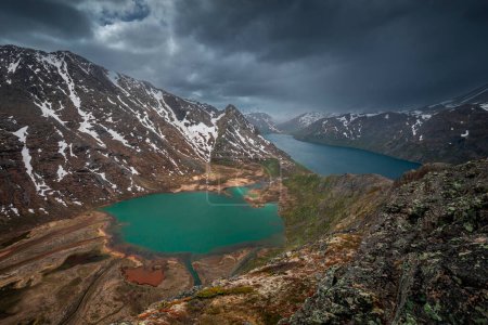 Foto de Turquoise and blue lakes in mountain landscape from above the hike to Knutshoe summit in Jotunheimen National Park in Norway, mountains of Besseggen in background, dramatic cloudy sky with rain - Imagen libre de derechos