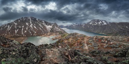 Foto de Turquoise and blue lakes in mountain landscape from above the hike to Knutshoe summit in Jotunheimen National Park in Norway, mountains of Besseggen in background, dramatic cloudy sky with rain - Imagen libre de derechos