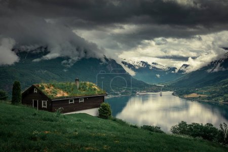 Téléchargez les photos : Grass roof wooden house over the Nordfjord fjord in summer in Norway, dark clouds over the mountains - en image libre de droit