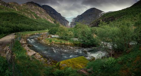 Téléchargez les photos : Mountain river with hiking path to Briksdalsbreen glacier in the mountains of Jostedalsbreen national park in Norway, moody atmosphere - en image libre de droit