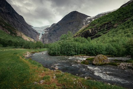 Foto de Mountain river with ice cold water of Briksdalsbreen glacier in the mountains of Jostedalsbreen national park in Norway, moody atmosphere, rocks in the water - Imagen libre de derechos