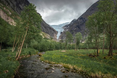 Foto de Mountain river with ice cold water of Briksdalsbreen glacier in the mountains of Jostedalsbreen national park in Norway, trees and meadows along the water - Imagen libre de derechos