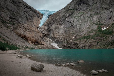 Téléchargez les photos : Briksdalsbreen glacier ice in the mountains of Jostedalsbreen national park in Norway, turquoise glacier lake, rocks along the beach - en image libre de droit