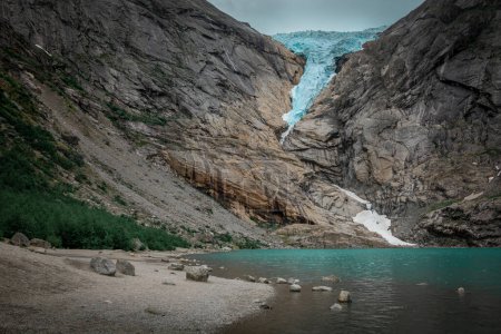 Téléchargez les photos : Briksdalsbreen glacier ice in the mountains of Jostedalsbreen national park in Norway, turquoise glacier lake, rocks along the beach - en image libre de droit