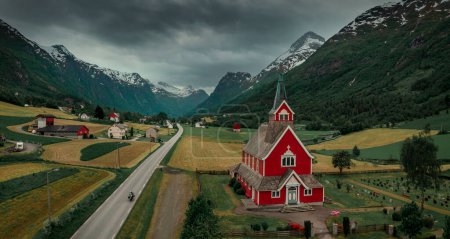 Foto de Red wooden church of Olden with road in the fjord Nordfjord in summer in Norway from above, motorcycle driving on highway, moody atmosphere in the mountains and sky - Imagen libre de derechos