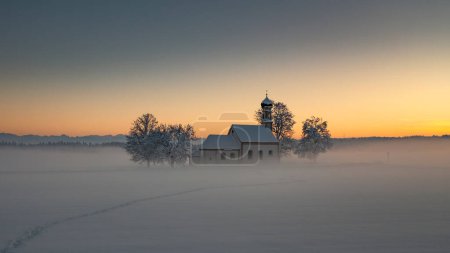 Foto de Bavarian church of Raisting with trees and snow during winter and sunset, snow field in the foreground, Bavaria Germany - Imagen libre de derechos