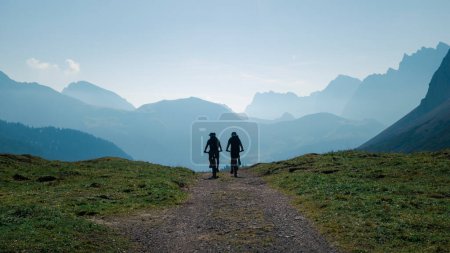 Silhouettes of two men mountainbiking in the Karwendel mountains in front of blue mountain layers during sunny blue sky day in summer, Tyrol Austria