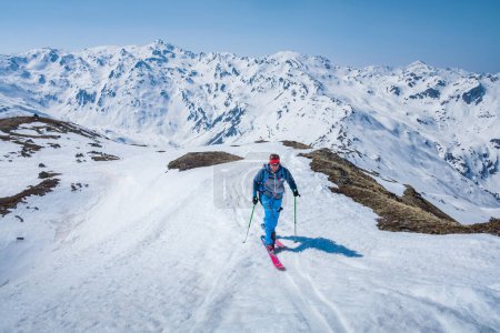 Hombre en esquí de montaña tour en la nieve en el día soleado, panorama de montaña de invierno en el fondo