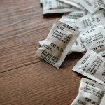 Desiccant or silica gel in white paper packaging on a wooden background.