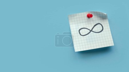 Infinity sign or symbol handwritten on a memo note over blue background.