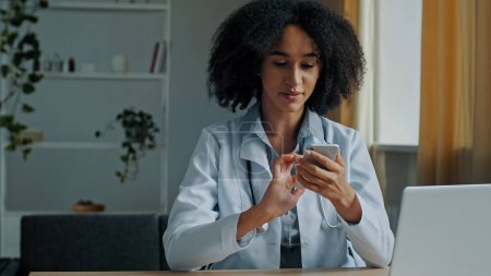 Téléchargez les photos : Médecin africain femme thérapeute utiliser téléphone portable app SMS message recommandation médicale pour la consultation des patients en ligne médecine de traitement à distance en temps de pandémie technologie moderne et soins de santé - en image libre de droit