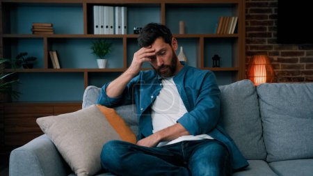 Photo for Tired upset father caucasian bearded man sit on sofa frustrated about hard working day at home stressed worried single guy lonely male irritated anxious feel unwell exhaistion lack of energy stress - Royalty Free Image