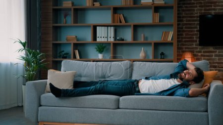 Téléchargez les photos : Homme caucasien épuisé sautant sur un canapé doux dans le salon tombant sur un canapé confortable profiter de la sieste quotidienne repos sain après la journée de travail a du plaisir temps de détente week-end sans soucis à la maison seul - en image libre de droit