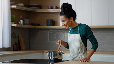 Téléchargez les photos : Femme chef arabian femme cuisinière femme cuisine plat aromatique sur cuisinière à la maison cuisine préparer des aliments sains avec des ingrédients naturels frais mélanger soupe repas chaud matin petit déjeuner passe-temps culinaire - en image libre de droit