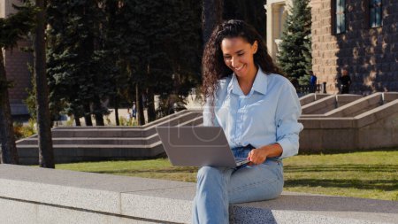 Photo for Smiling happy cheerful carefree young girl student winner successful business woman with laptop sitting in city street rejoicing chatting online receives good news winning watching funny video smiles - Royalty Free Image
