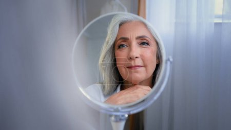 Photo for Mirror reflection female wrinkled face 50s middle-aged Caucasian woman senior lady looking self lover skin care grandmother thinking pampering mirrored soft facial beauty cosmetology rejuvenation - Royalty Free Image