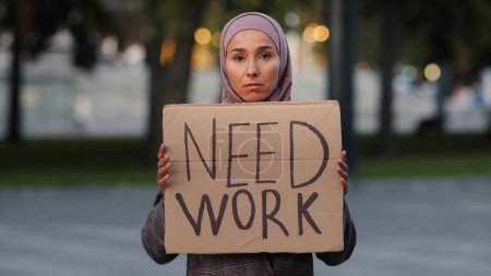 Téléchargez les photos : Triste femme musulmane dans le hijab debout à l'extérieur fille ethnique islamique bouleversé au chômage inquiet dame stressante pauvre femme montrant tenant panneau de bannière en carton besoin de travail, licenciement crise covide pandémique. Haut - en image libre de droit