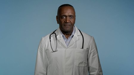 Photo for Mature confident happy doctor standing in gray background studio with arms crossed glad smiling african american man professional therapist physician in medical gown posing indoors looking at camera - Royalty Free Image