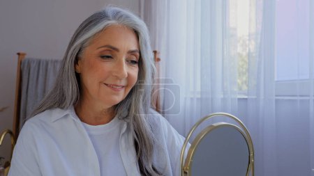 Téléchargez les photos : Caucasien souriant belle vieille dame âgée mature vieille femme modèle avec cheveux gris femelle regardant miroir reflet sourire regarder rides visage peau lisse naturel visage beauté teint - en image libre de droit