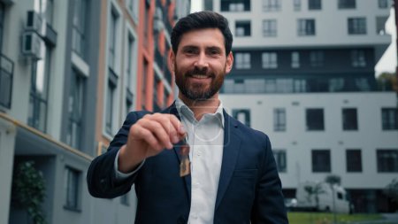 Happy homeowner realtor estate agent business man holding keys of new skyscraper dwelling rental apartment in downtown advertising office buildings sold house in modern district city selling property