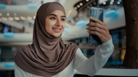 Photo for Islamic muslim lady beautiful woman in hijab hold modern gadget talk phone look at webcam chatting online mobile video call arabian girl shopper recording blog from shopping center live broadcasting - Royalty Free Image
